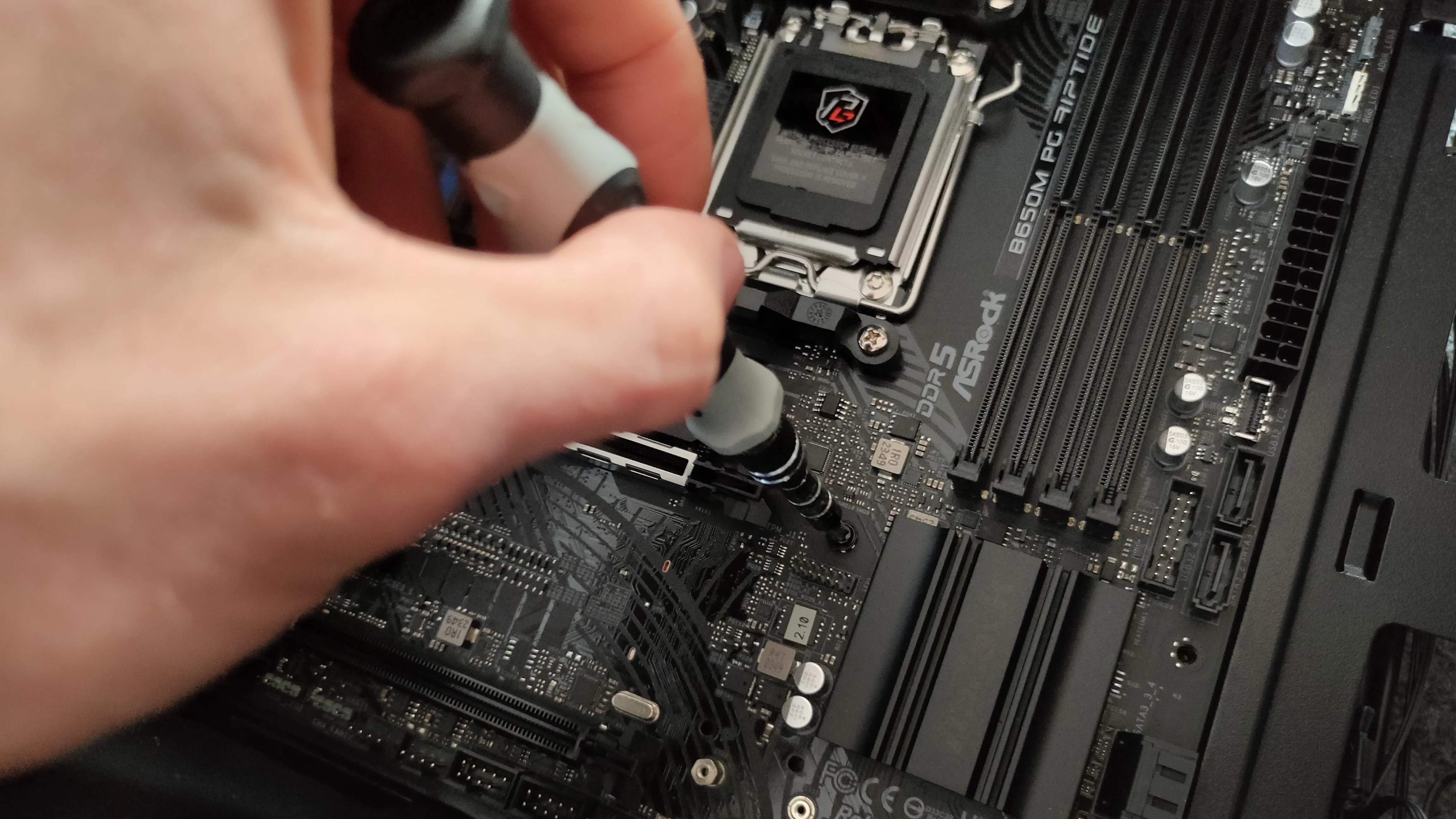 Bàn tay đang siết chặt ốc vít cố định bo mạch chủ vào vỏ case PC, biểu tượng của quá trình lắp ráp linh kiện.