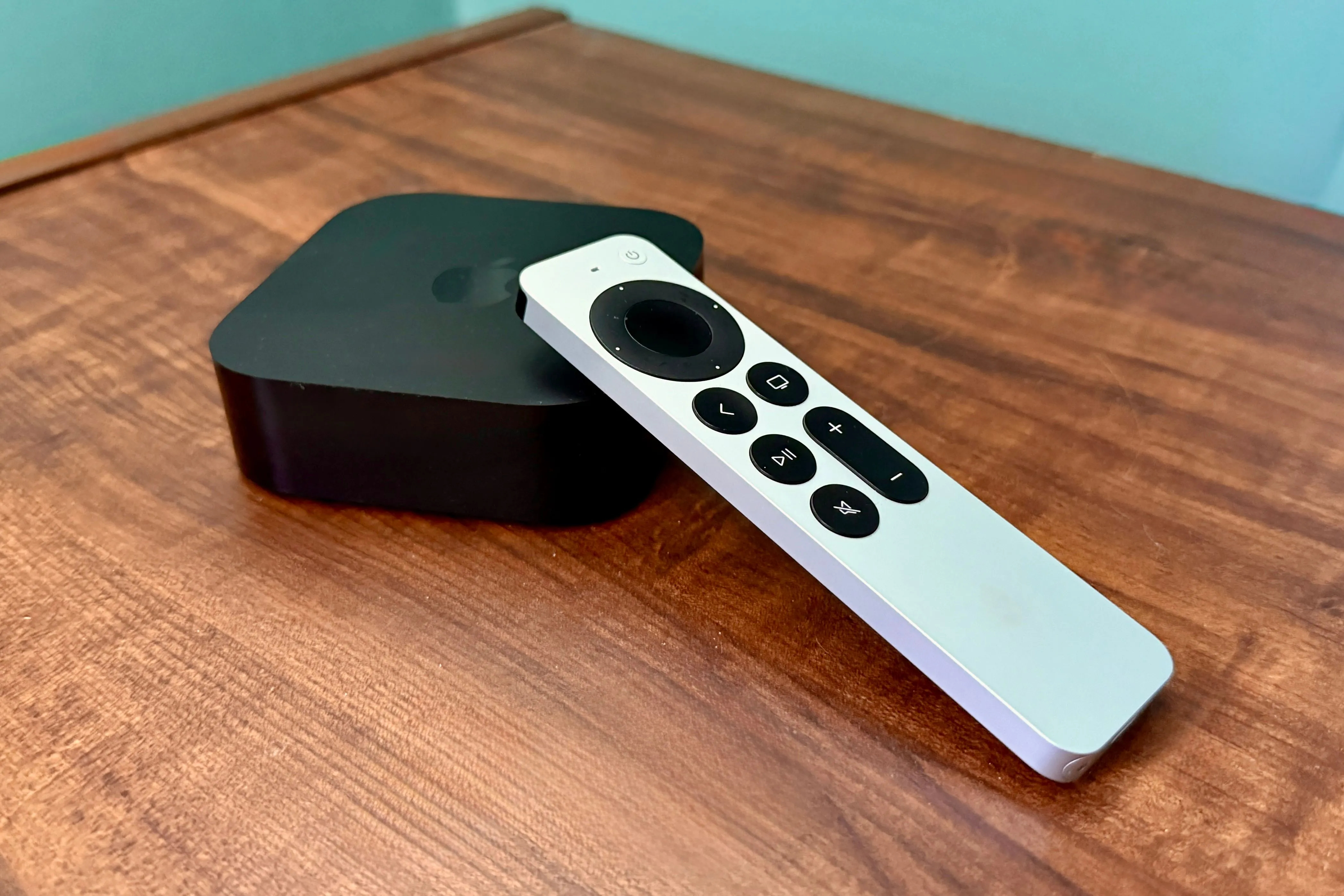 Bộ điều khiển và Apple TV 4K nằm trên mặt bàn gỗ, thể hiện sự nhỏ gọn của thiết bị giải trí.