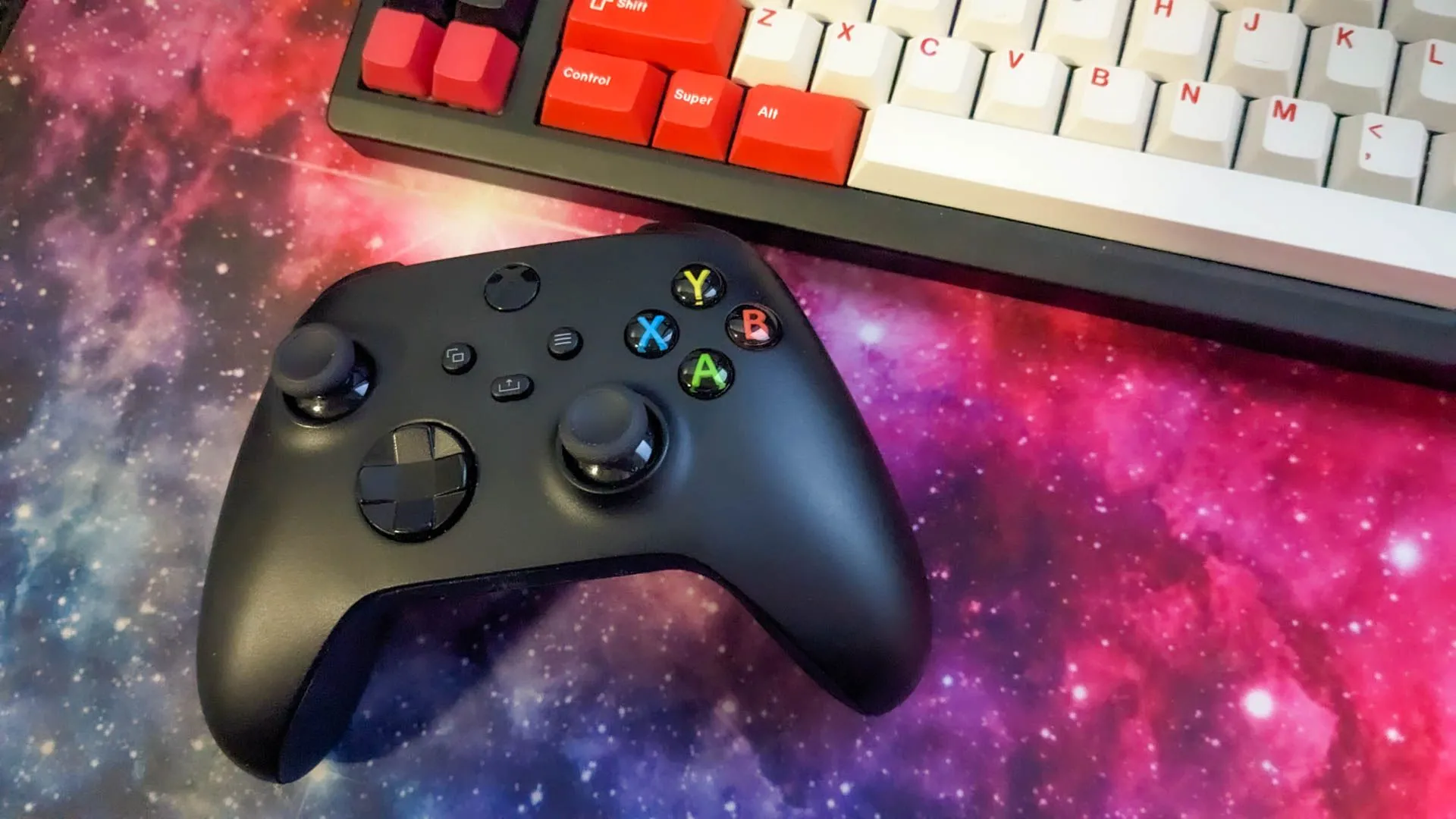 Bộ điều khiển Xbox cạnh bàn phím cơ trên tấm lót chuột không gian. Biểu trưng cho không gian gaming đa dạng và các lựa chọn phụ kiện khác ngoài tấm lót chuột kính.
