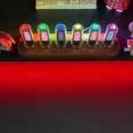 Chân đế Razer Monitor Stand Chroma hiển thị ánh sáng RGB đỏ nổi bật dưới gầm, xung quanh là các phụ kiện công nghệ