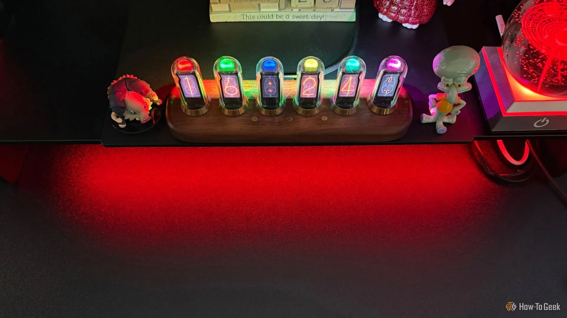 Chân đế Razer Monitor Stand Chroma hiển thị ánh sáng RGB đỏ nổi bật dưới gầm, xung quanh là các phụ kiện công nghệ