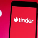 Điện thoại thông minh hiển thị logo ứng dụng Tinder trên nền đỏ, minh họa về hẹn hò trực tuyến.