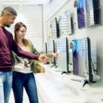 Hai người đang xem xét một chiếc TV lớn tại cửa hàng điện máy, thể hiện trải nghiệm mua sắm trực tiếp.