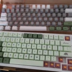 Hình ảnh bàn phím Ajazz AK820 Pro với keycap màu xanh lá tùy chỉnh đang được lắp đặt và bộ keycap gốc ở trên.