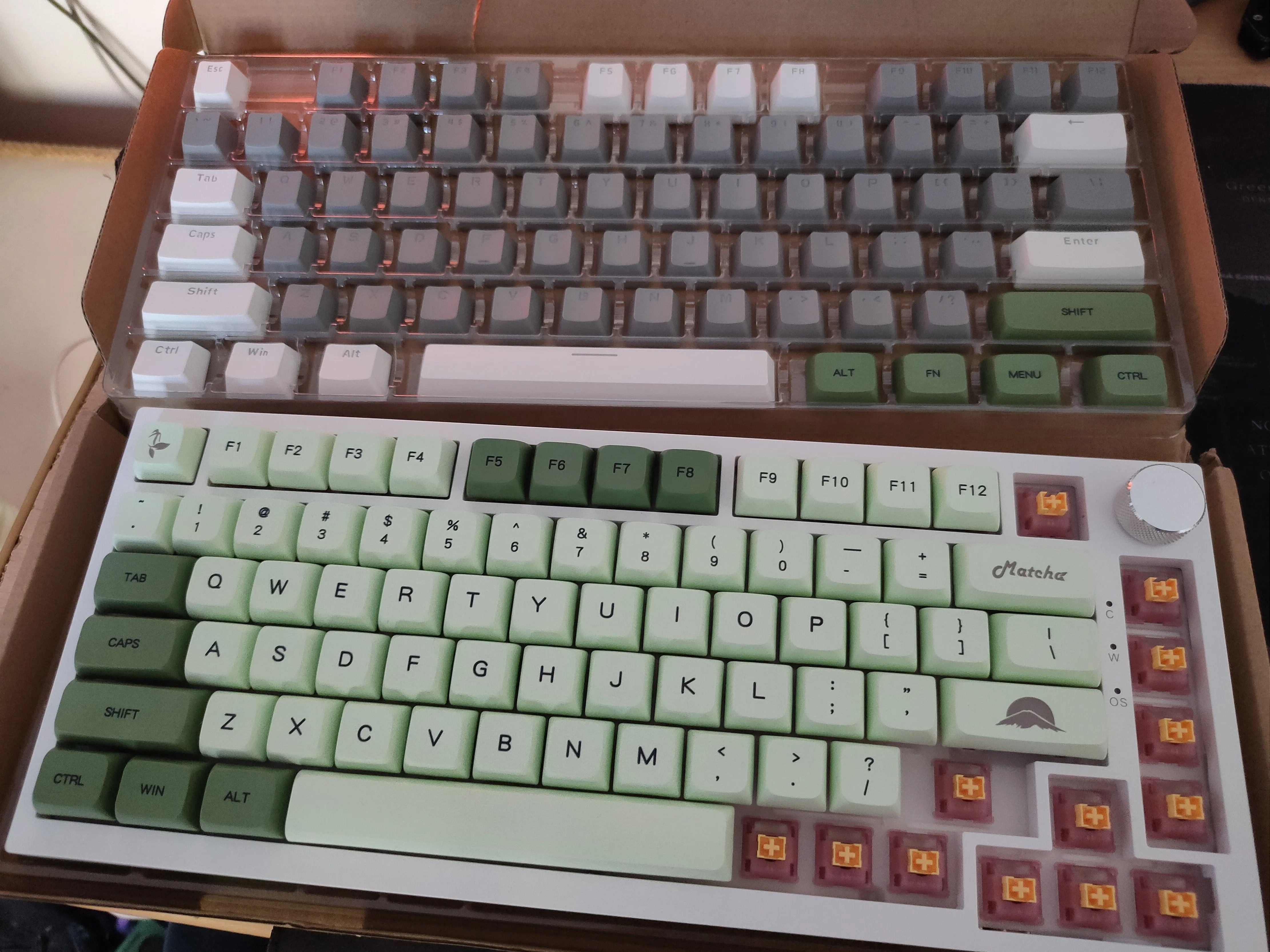 Hình ảnh bàn phím Ajazz AK820 Pro với keycap màu xanh lá tùy chỉnh đang được lắp đặt và bộ keycap gốc ở trên.