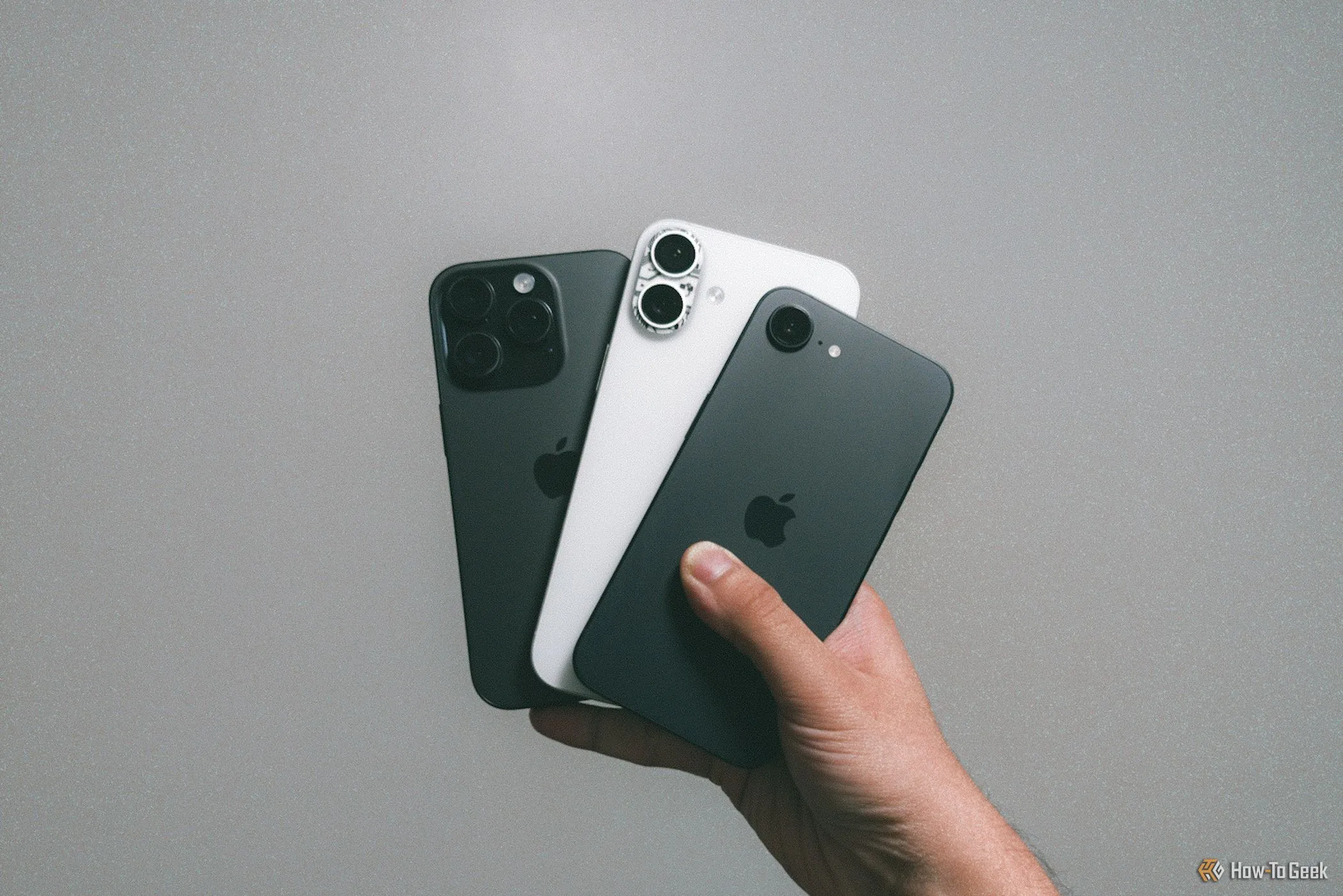 Mẫu iPhone 16e, iPhone 16 Plus và iPhone 16 Pro được cầm trên tay trước bức tường màu xám, biểu tượng của sự đồng nhất trong thiết kế smartphone hiện đại.