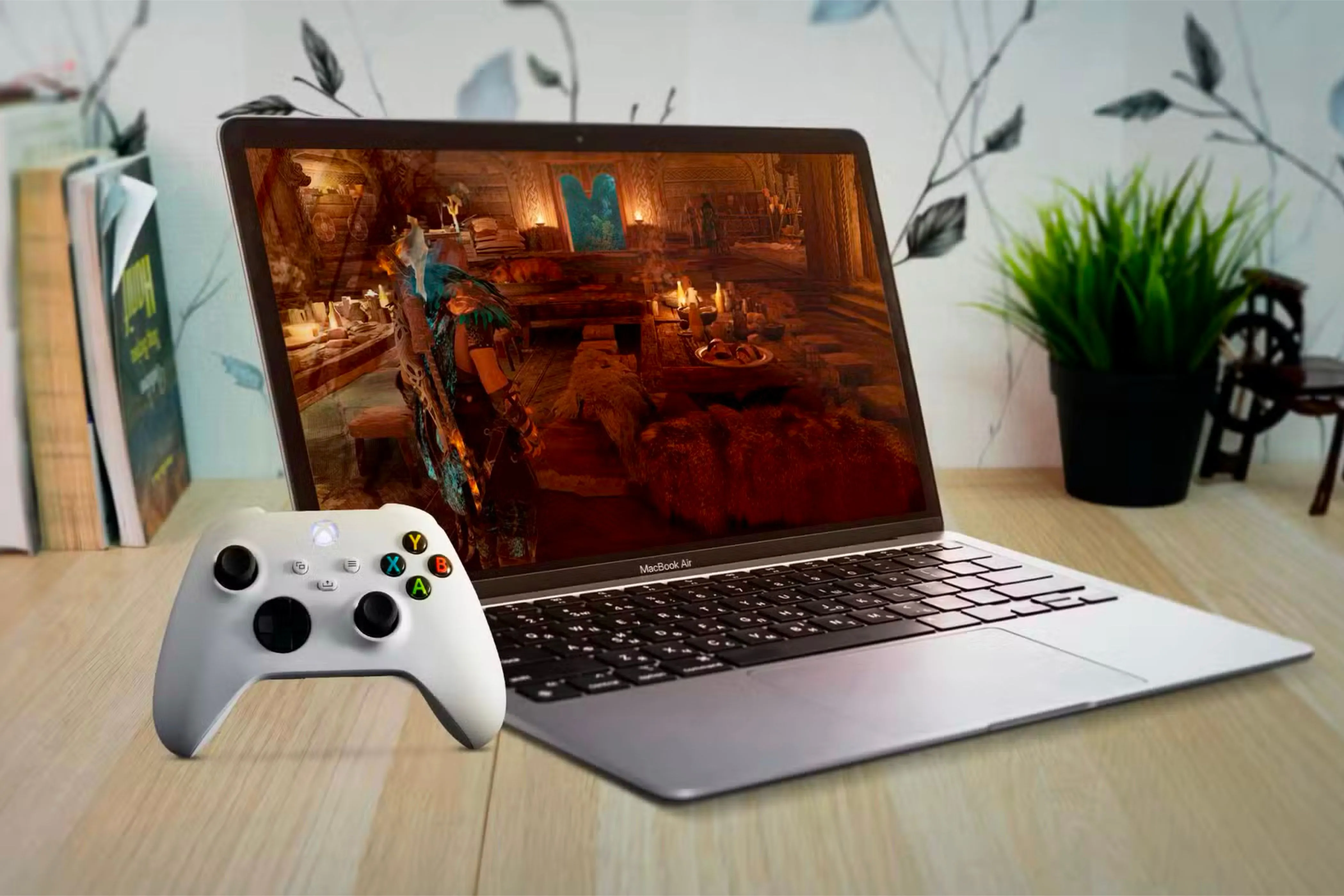 Một chiếc MacBook Air đặt dưới bàn gỗ với màn hình hiển thị game và tay cầm Xbox bên trái.