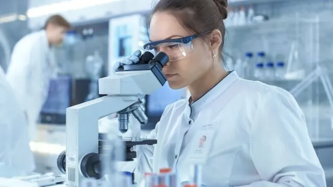 Một nhà khoa học trong phòng thí nghiệm đang nhìn qua kính hiển vi