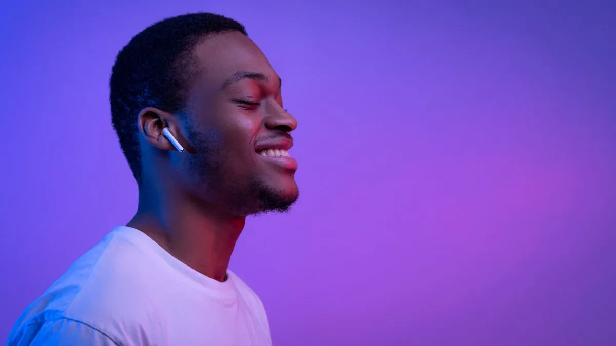 Người đàn ông thư giãn đeo tai nghe Apple AirPods, minh họa việc nghe nhạc hoặc thiền mà không cần nhìn vào màn hình điện thoại.