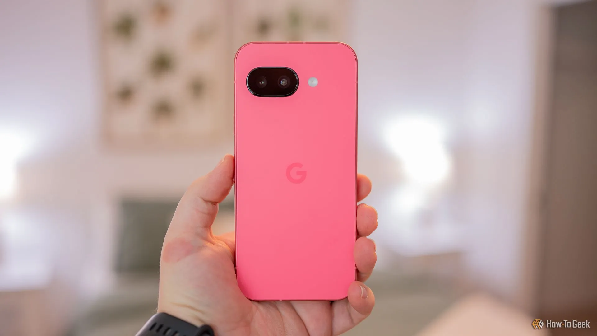 Người dùng cầm điện thoại Google Pixel 9a màu hồng Peony, làm nổi bật mặt lưng và cụm camera được thiết kế lại, cho thấy sự thay đổi đáng kể về thẩm mỹ của dòng Pixel A