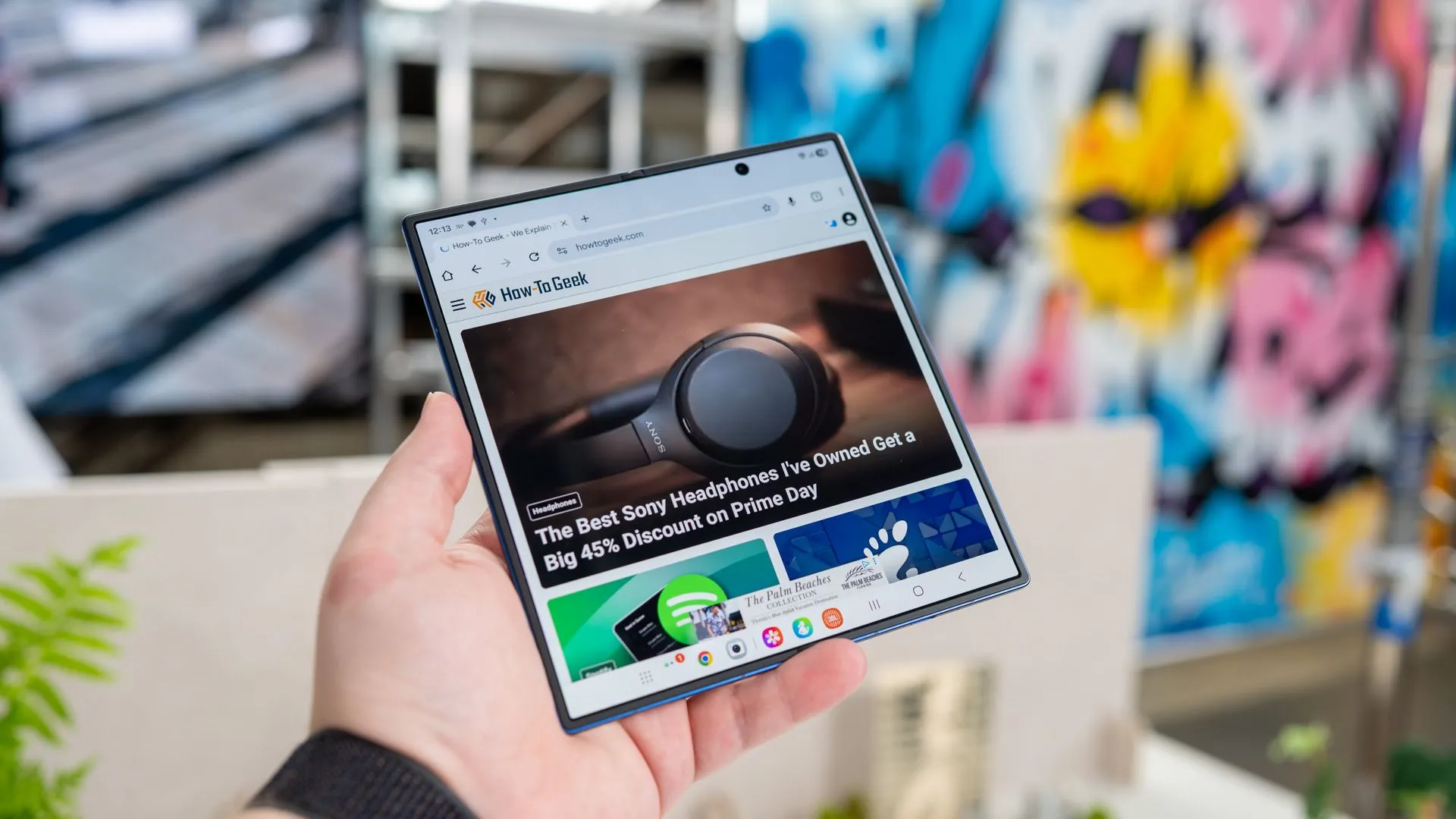 Người dùng đang cầm Samsung Galaxy Z Fold 7 mở ra, hiển thị trang web How-To Geek trên màn hình chính