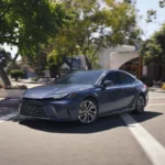 Ô tô Toyota Camry 2026 màu xám bạc di chuyển trên đường phố, thể hiện thiết kế "đầu búa" và đèn LED hiện đại.