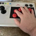 Tay cầm Arcade 8BitDo được đặt cạnh bàn tay người dùng để minh họa kích thước và thiết kế công thái học.