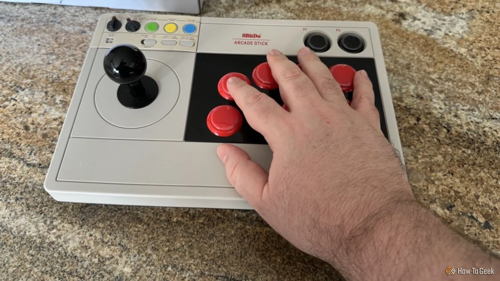 Tay cầm Arcade 8BitDo được đặt cạnh bàn tay người dùng để minh họa kích thước và thiết kế công thái học.