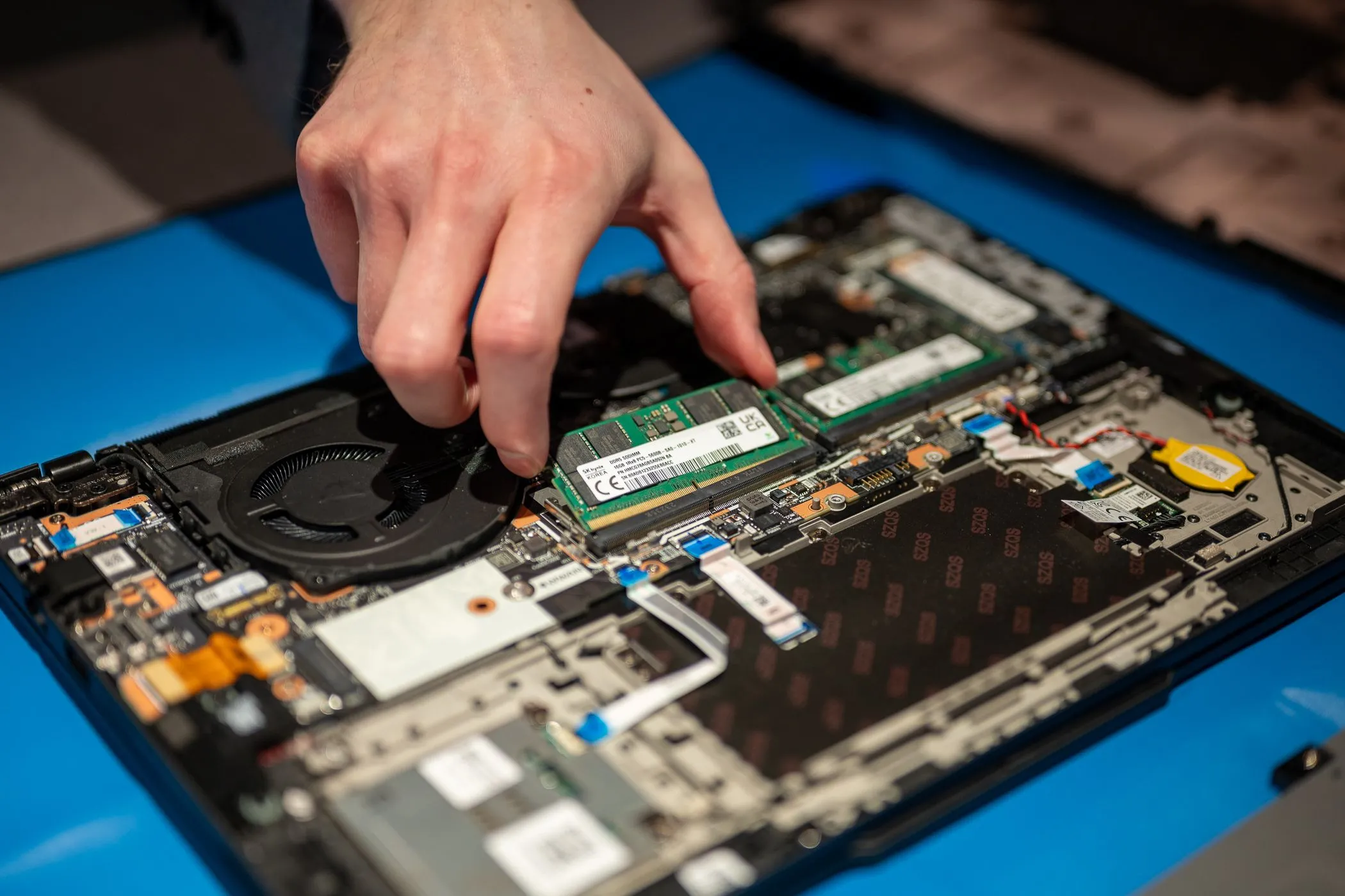 Thợ kỹ thuật đang nâng cấp RAM cho laptop Lenovo, cho thấy bo mạch chủ và các linh kiện bên trong. Hình ảnh minh họa việc nâng cấp phần cứng máy tính cũ để tối ưu hiệu suất.